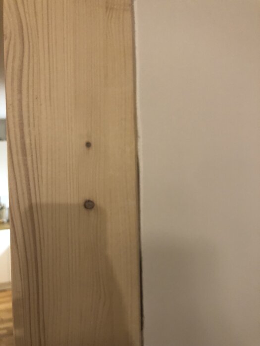 Gränsen mellan en limträpelare och en bredspacklad vägg med synliga skarvar.