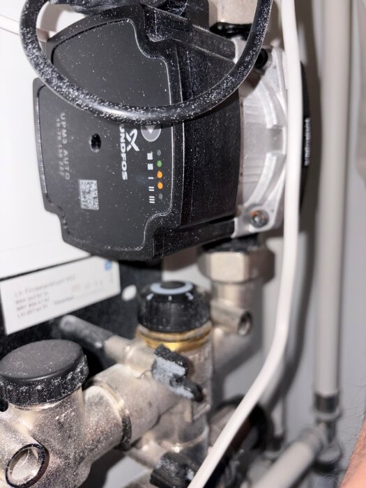 Cirkulationspump från Grundfos med rör och kablar i ett tekniskt utrymme, visar anslutningar och märkning.