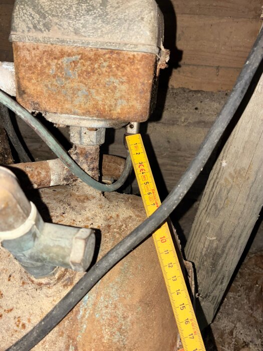 Rostig kompressor med måttband och synlig ventil där luft läcker, belägen i träbeklädd miljö.