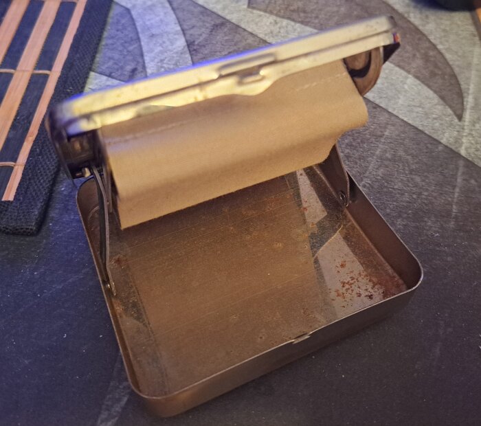 Gammaldags cigarettmaskin med rostig botten och metallram som håller brunt papper.