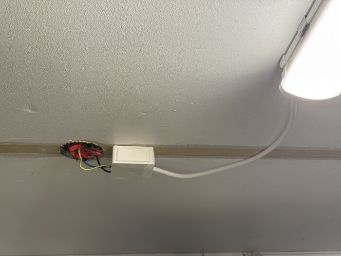 Kablage och kopplingsdosa i taket med lysrörsarmatur, kablar hänger synligt utan täckning runt hålet där de är kopplade.