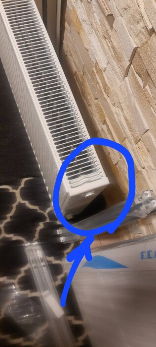 Radiator vid vägg med betongsten; blå cirkel markerar anslutning för värmerör.