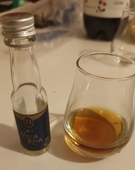 En liten flaska med mörk rom, märkt "Villa Rica 23 Years", står bredvid ett glas med bärnstensfärgad vätska på ett bord.