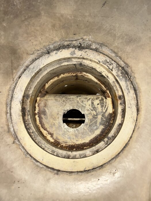 Rostigt och smutsigt vattenlås i tvättstuga med runt lock och hål i mitten, före rengöring.