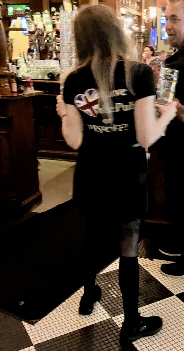 En person i en pubmiljö bär en ölstånka, med en tröja dekorerad med en brittisk flagga.