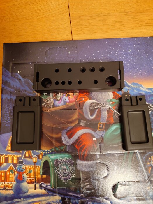 Svarta monteringsdelar placerade ovanpå en julkalender med tomtemotiv och vinterlandskap.