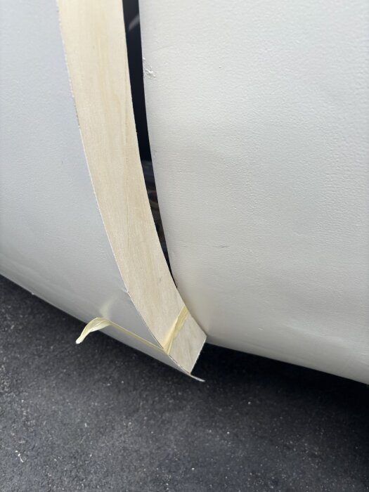 Twistad träbit monterad på dörrkarm, fixerad med tejp. Dörrens ram och karm avviker från varandra, arbete pågår med justering.