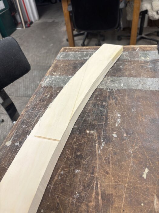 En träbit med märkningar för sågning eller snitt ligger på ett arbetsbord i en verkstad för byggprojekt.