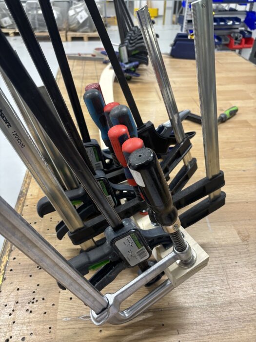 Träbitar klämmade med tvingar på en arbetsbänk under modifieringsarbete av dörrkarmen, omgivna av verktyg och material i bakgrunden.