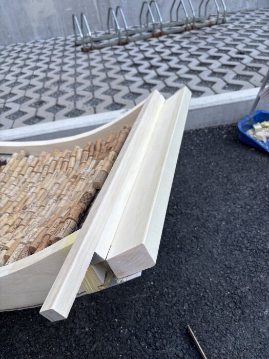 Träbitar och vinkorkar sammanfogade på marken, del av renoveringsprojekt för dörrkarm med komplex passform. Bakgrund i mönstrade plattor och cykelställ.