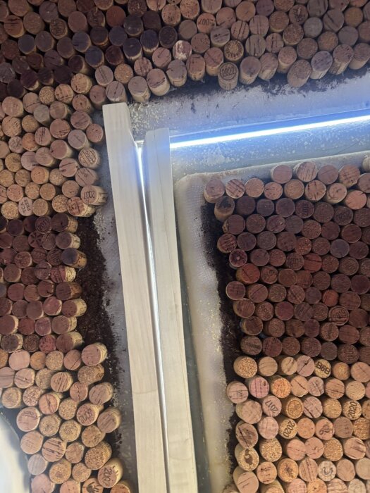 Trävägg med vinkorkar inbäddade i kork-silikon komposit, ljuslist ovanför och två träbitar inpassade i öppningen.