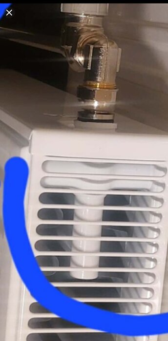 Närbild av en radiator med monterad ventilkoppel och misstänkt luftningsnippel, fotograferad framifrån med en blå markering.