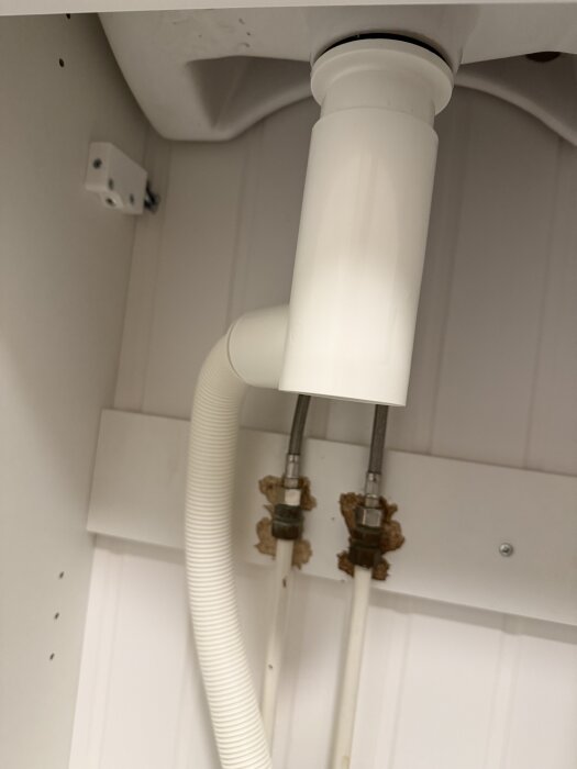 Under diskbänk med vita avloppsrör och anslutningar, med fokus på ett Prevex vattenlås och misstänkt läckage från en gummiring.