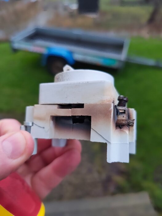 Bränd och skadad strömbrytare i närbild, hålls i en hand, med mörka märken och sprickor.