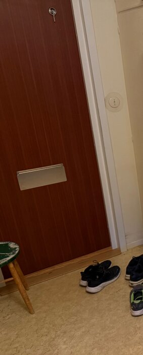 Ingångsparti med en dörr, en gammal plastmatta och några par skor på golvet i en hall.