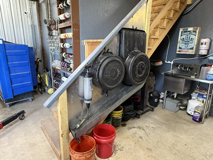 Verkstad med trappa, verktygshylla, färgburkar, och tvättho.