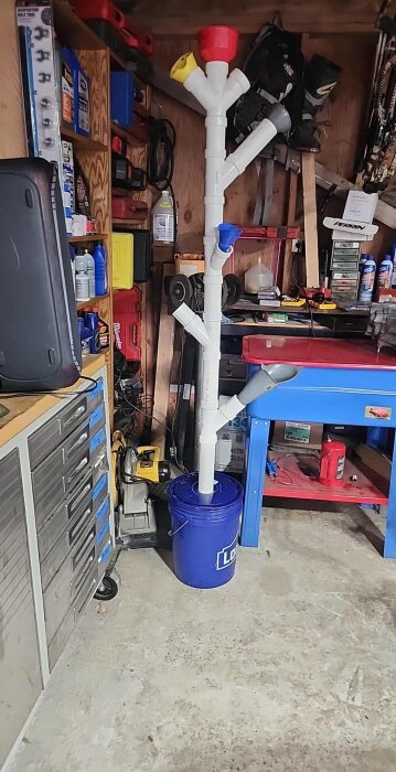 DIY-trattar i plast installerade på PVC-rör kopplade till en blå hink i ett garage fyllt med verktyg och förnödenheter.