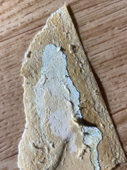 Rivet lager av gammal tapet påträffat vid renovering, med strukturerad yta och skiktad färg, möjligt inslag av äldre material som asbest.