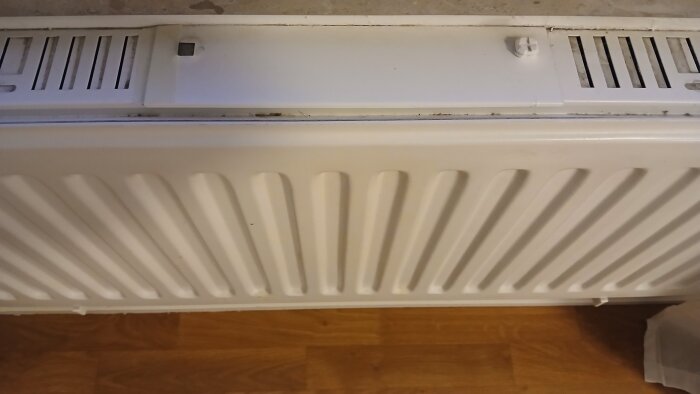 Radiator med locket i mitten öppnat för att visa platsen där filtret sitter, ovanpå trägolv.