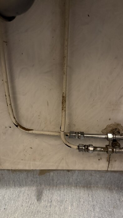 Rörsystem i tvättstuga eller kök med smutsiga vita rör och metallkopplingar, bilden visar närbild av installationen.
