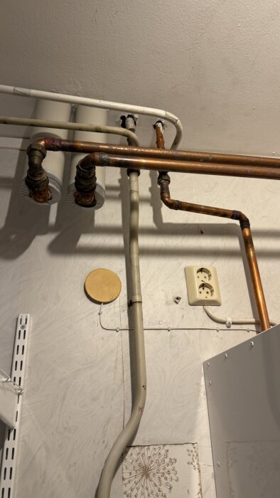 Rörsystem i tvättstugan med koppar- och plaströr monterade på en vägg, samt ett eluttag.