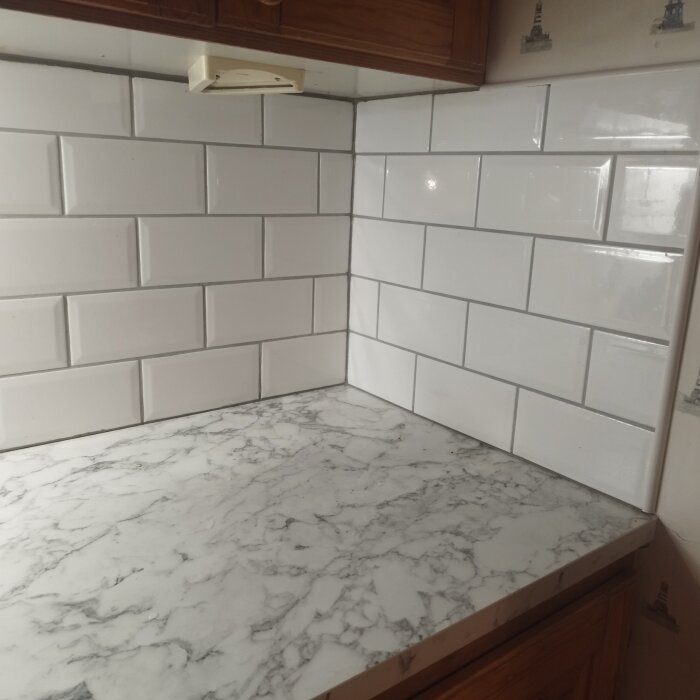 Vitt kakel monterat ovanför en marmorerad köksbänk, med ojämna fogar.