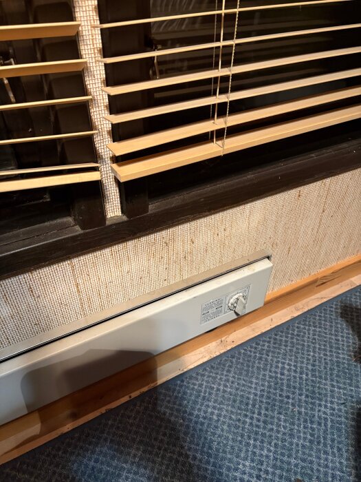 Vita 120 mm bred plåt med ram vid element under fönster med persienner, blå matta golv.