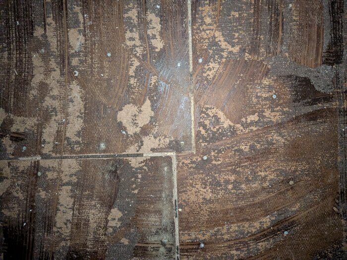 Gammal masonitskiva med spikar och limrester synlig efter rivning av plastmatta i ett 100-årigt hus.