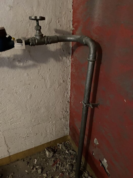Vattenledning med avstängningsventil i ett rum med rödmålade väggar, delvis rivet golv.