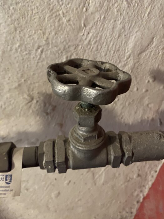 Ventil för inkommande vattenledning monterad mot en grovputsad vägg, visar ett stängt vred.