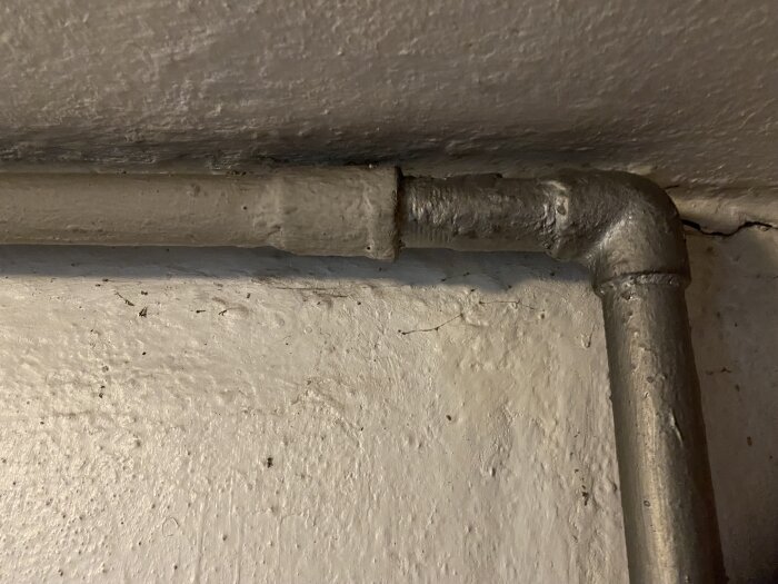 Närbild av en gammal vattenledning med en koppling mot en vit vägg, används för att diskutera byte av inkommande vattenrör vid dränering.