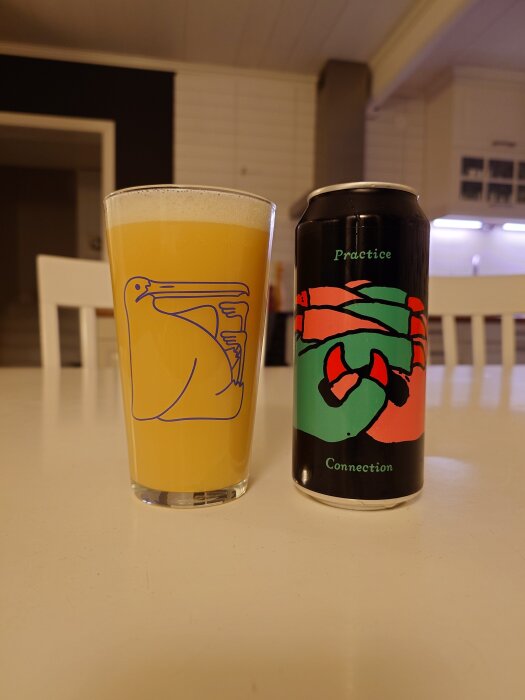 Ett glas med gyllengul öl bredvid en ölburk med färgglad design på ett bord i ett kök.