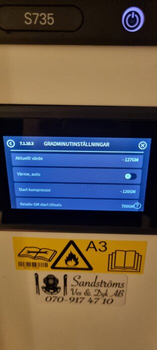 Närbild av en värmepumpsdisplay som visar gradminutinställningar med aktuella värden. En varningsskylt och företagslogga syns nedanför skärmen.