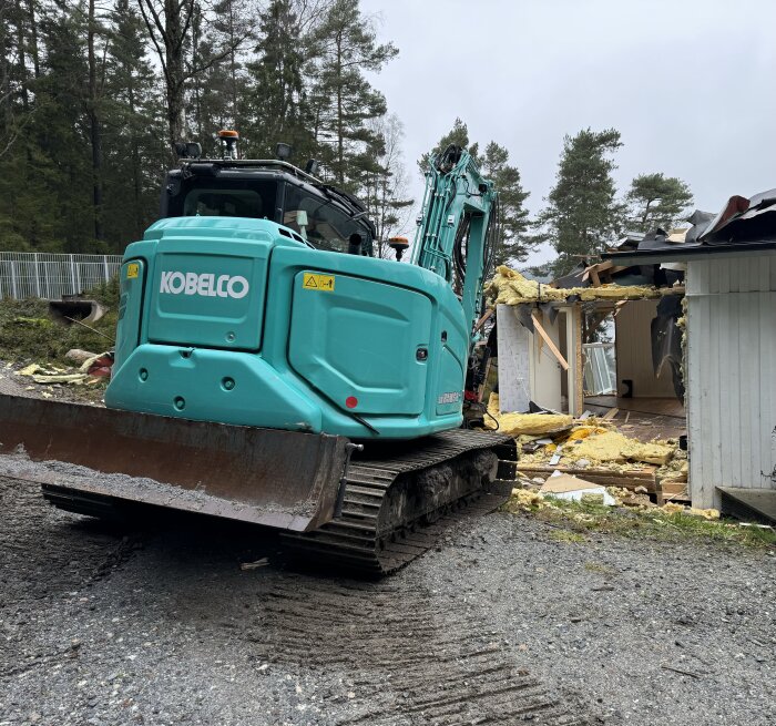 Grävmaskin från Kobelco river en gammal stuga, områdets omgivningar är skog och mark.