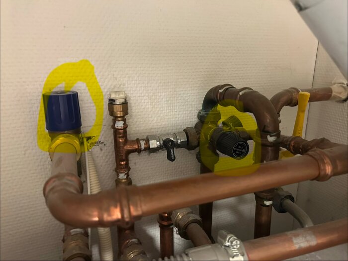 VVS-installation med kopparrör och ventiler, varav en blå och en svart är markerade med gult.