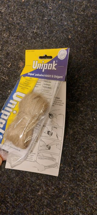 Förpackning med Unipak paksalve/rörkitt och unigarn på golv med instruktioner.