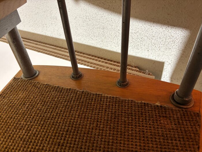 Ett trappsteg i trä med sliten brun matta och metallstänger från en spiraltrappa.