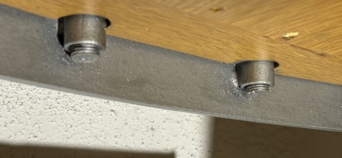 Trappsteg i spiraltrappa med synliga bultar och trägolv; fokus på underkonstruktion med metallstänger.