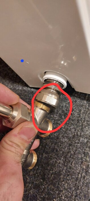 Hand som håller i en koppling som fäster in i ett element med en röd cirkel markerande området runt muttern på kopplingen.