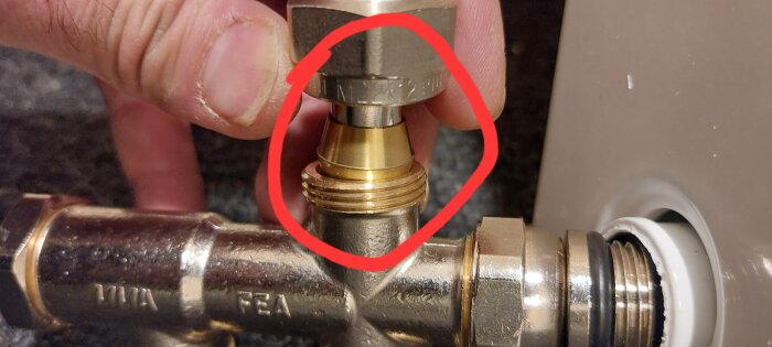 Närbild på en hand som håller i en rördel med ett ihopkopplingsområde markerat med en röd cirkel.