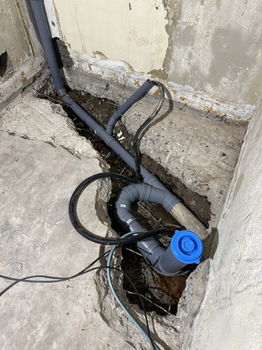 Renovering av källare, rörledningar installerade i uppbilad platta, provisorisk pumpbrunn synlig för att hantera vatten under plattan.