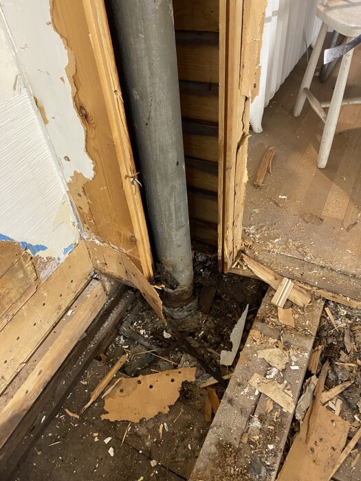 Sprucket avloppsrör och trasigt bjälklag synligt under rivning, omgiven av träflisor och skräp.