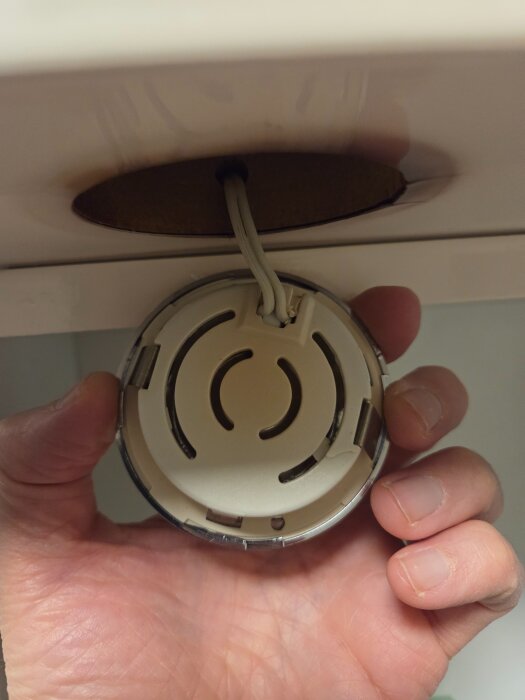 En hand håller en spotlampa utan synlig märkning, kopplad till ett kabelhål under ett skåp i ett badrum.