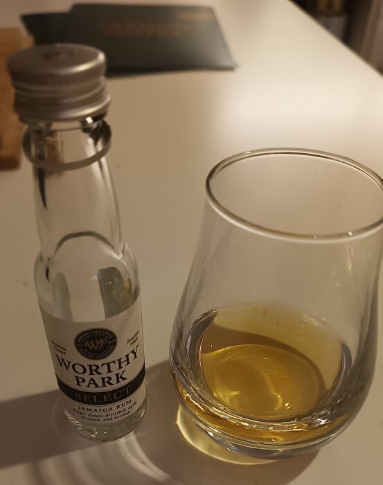 Flaska och glas med ljus rom på ett bord, etiketten visar "Worthy Park Select Jamaica Rum".