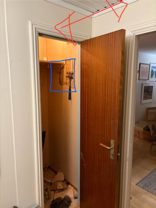 Dörröppning med delvis rivet väggområde markerat i blått, taknockens riktning markerad med röd pil, verktyg hänger på väggen.