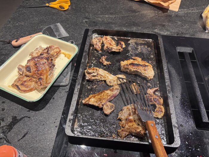 Gjutjärnsstekhäll med stekta köttbitar och kött i en form bredvid; stekspade på hällen.