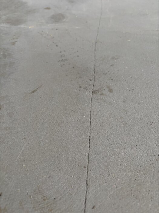 Spricka i spacklat golv som syns i närbild, oro över att slangen kan kännas under ytan och sprickor vid varje regel i bjälklaget.