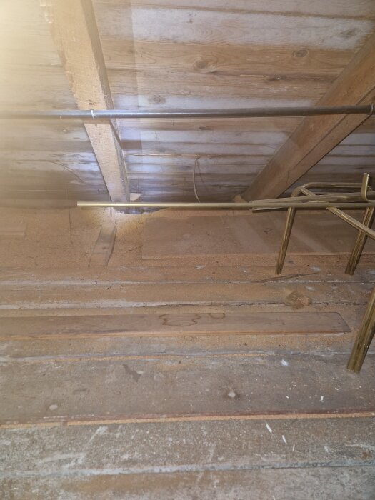 Vindvåning med synliga träbjälkar och rör, spår av fukt och mögel på norrsidan av taket synliga.