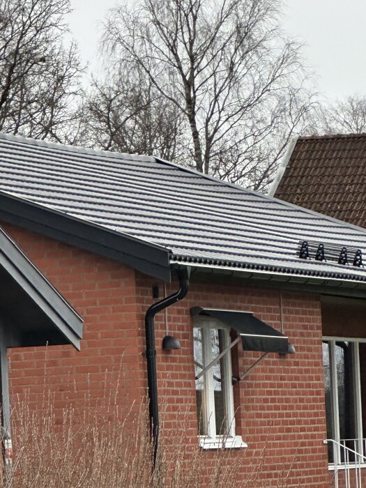 Rött tegelhus med nytt tak; ojämn taklinje tydligt synlig.