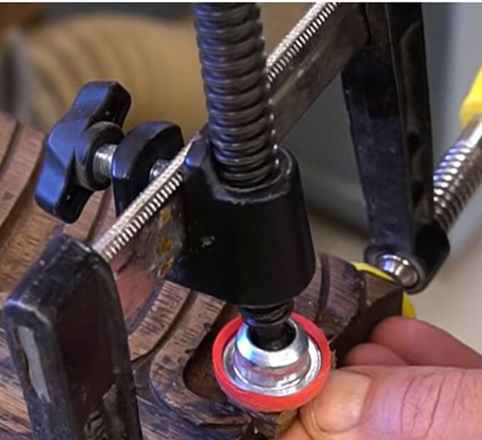 Ett tving med tillbehör för 90-graders tryck, svart vred och röd fot, används på en träbit.